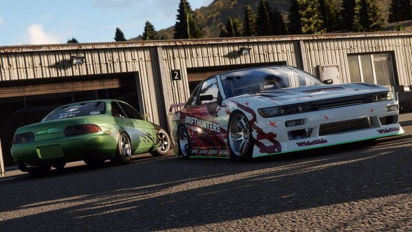 Screenshot from CarX Drift Racing Online showing two customized cars parked near a garage with trees and hills in the background.